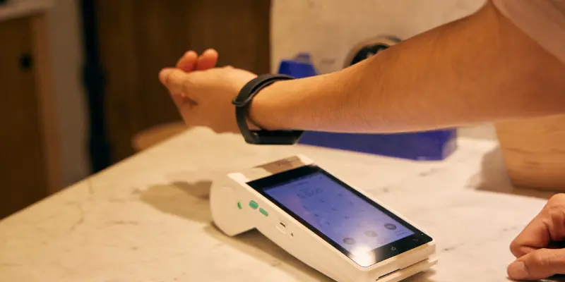Person making a contactless payment with a smartwatch at a payment terminal, showing NFC smartwatch payment feature.